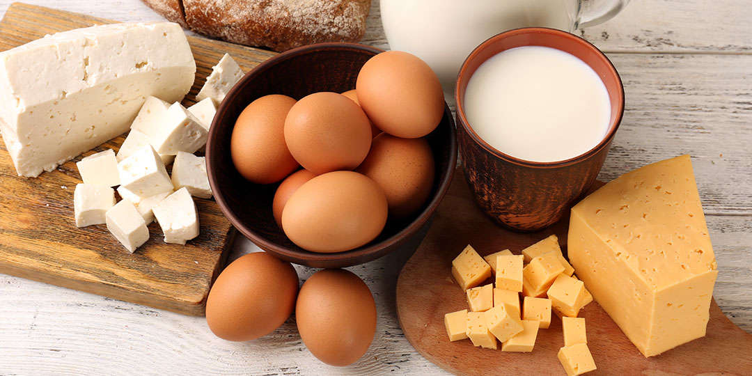 brown eggs in a bowl, white cheese and cheddar cheese on wooden cutting block, glass of milk